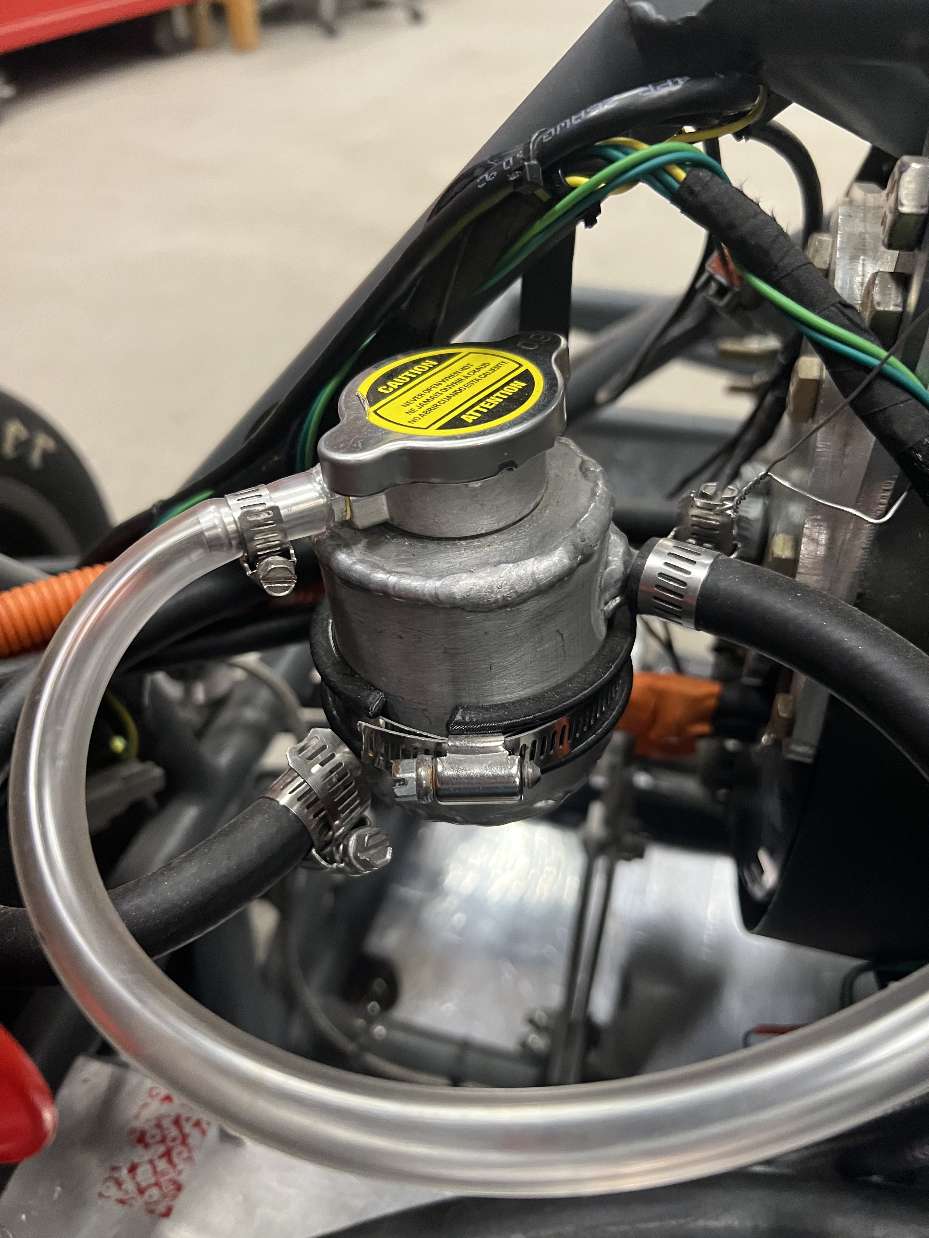 The welded aluminum swirl pot mounted in the car, topped with a pressure cap and connected to the coolant hoses by worm-drive clamps