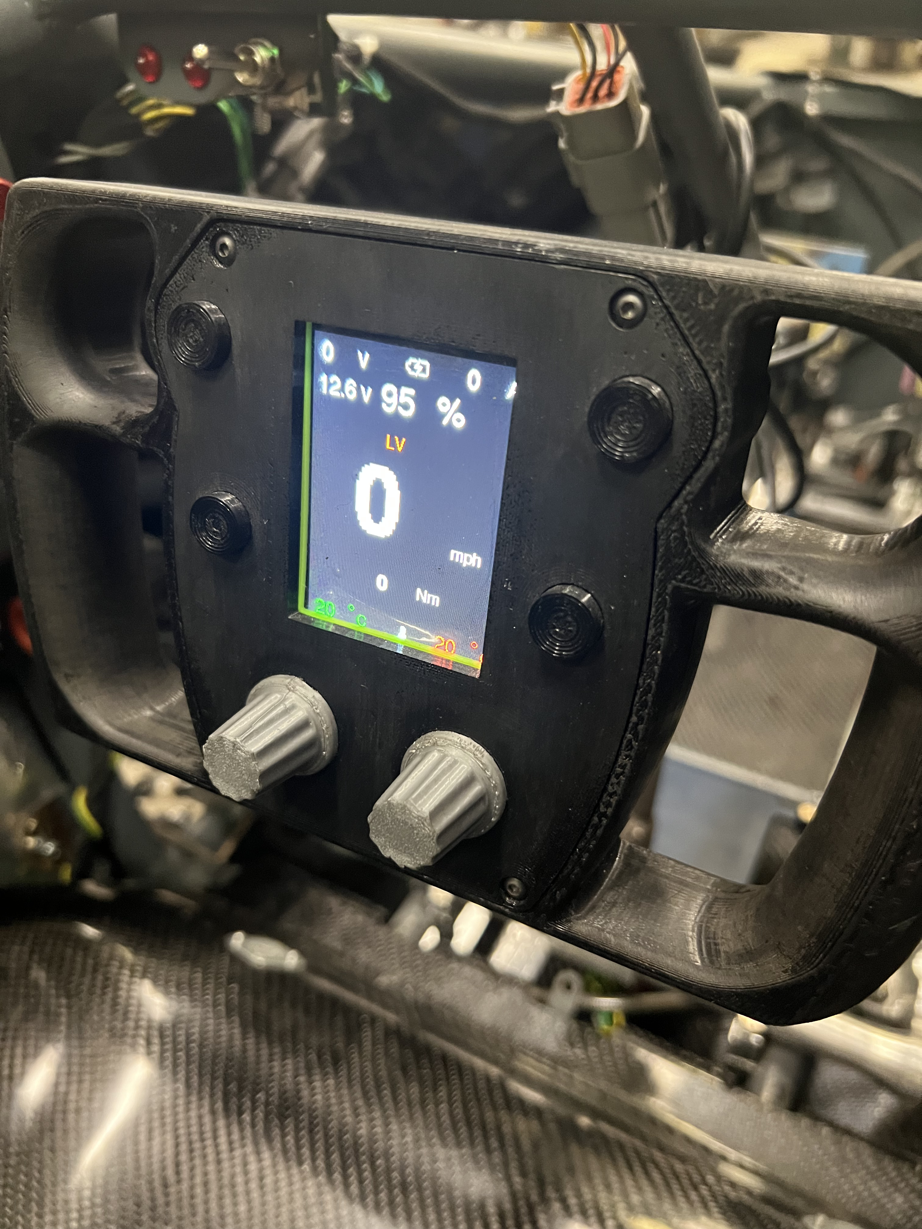 The dash display mounted in the car's steering wheel, lit up with voltage, percentage, speed and torque readouts