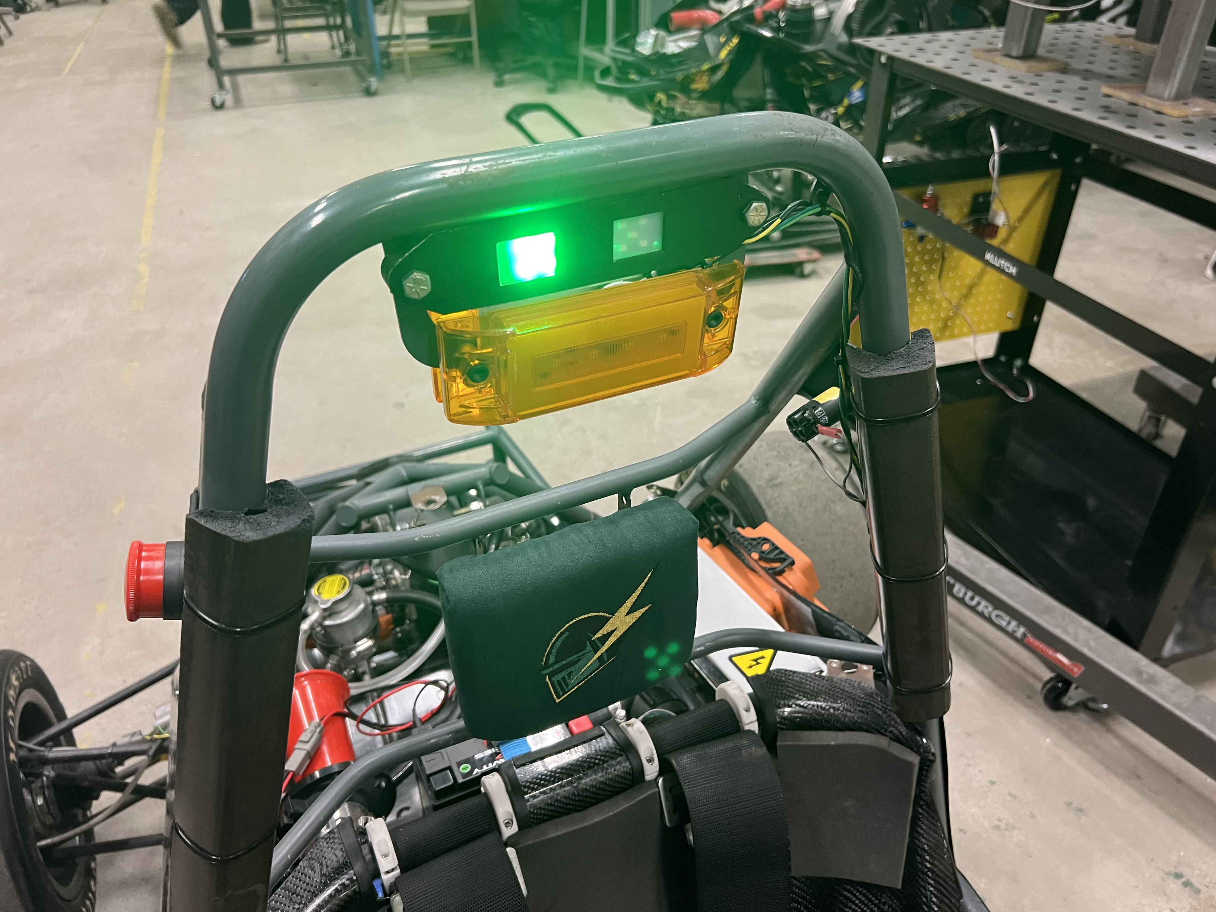 The car's roll hoop from behind, with a lit green indicator and an amber lens mounted to a bracket between the hoop's uprights