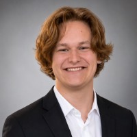 Greyson Howard in a dark suit jacket and white shirt, against a grey backdrop